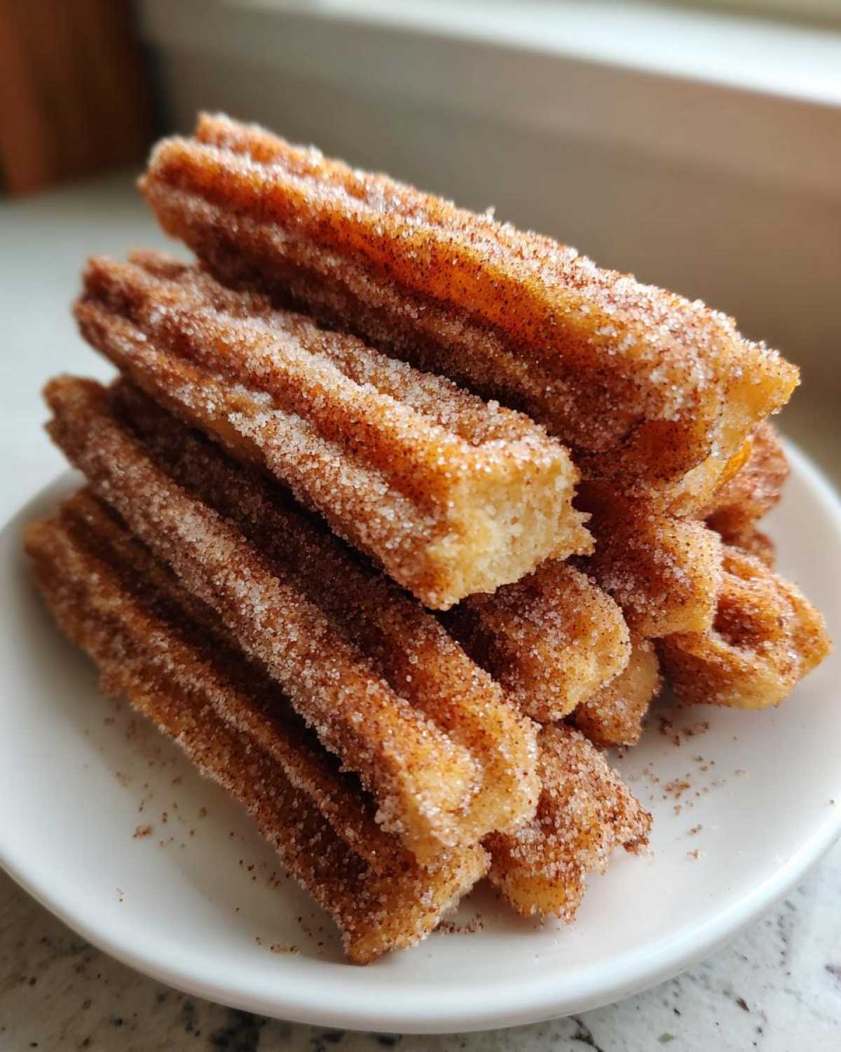 A stack of freshly made Gluten-Free Cinnamon Sugar Waffle Sticks coated heavily in cinnamon sugar on a white plate.