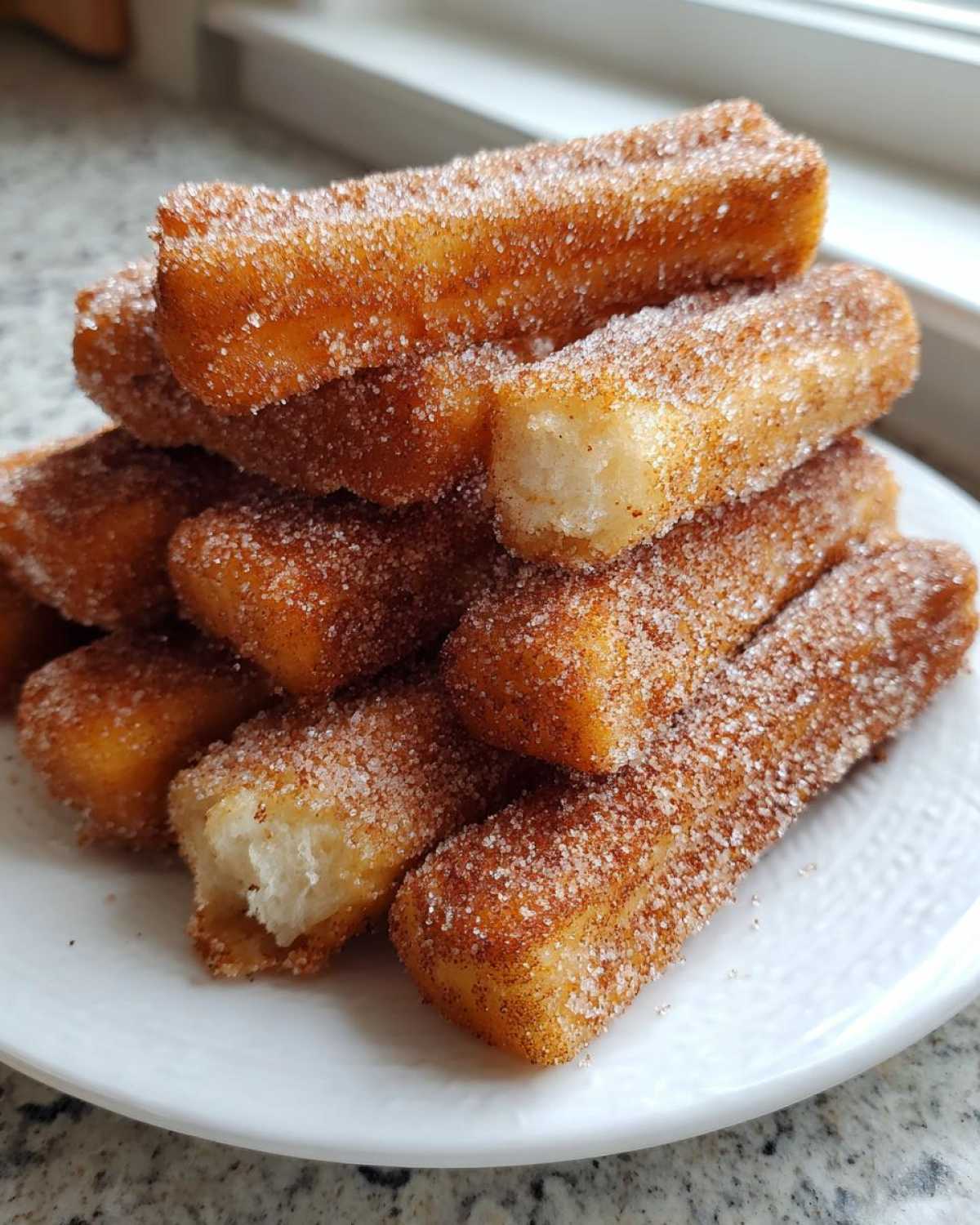 A close-up stack of golden Gluten-Free Cinnamon Sugar Waffle Sticks coated heavily in cinnamon sugar on a white plate.