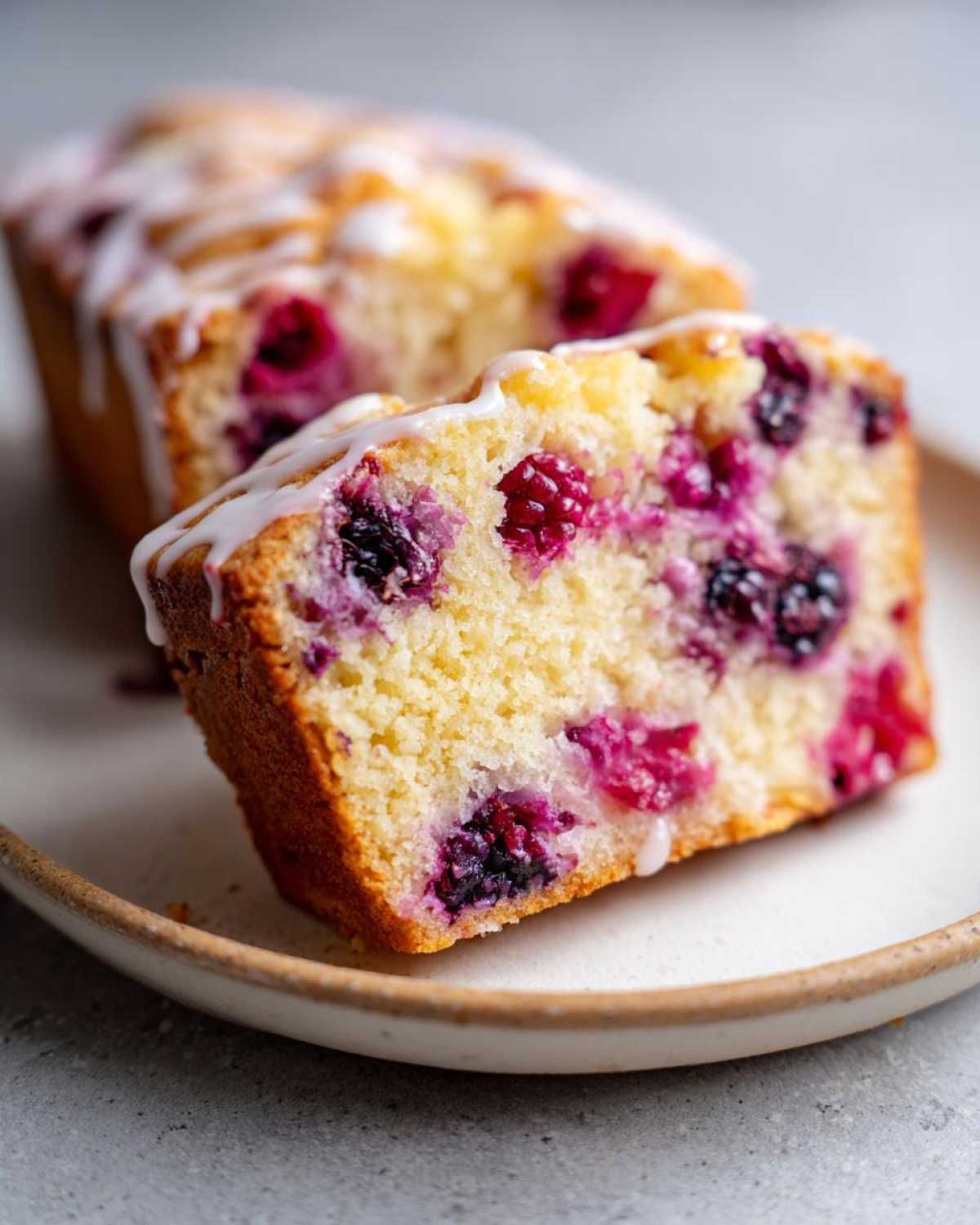 Close-up of a slice of Gluten-Free Lemon Berry Yogurt Cake showing moist crumb and mixed berries, drizzled with white icing.