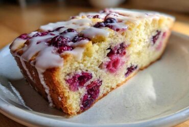 A close-up of a moist slice of Gluten-Free Lemon Berry Yogurt Cake topped with a white lemon glaze and baked-in berries.