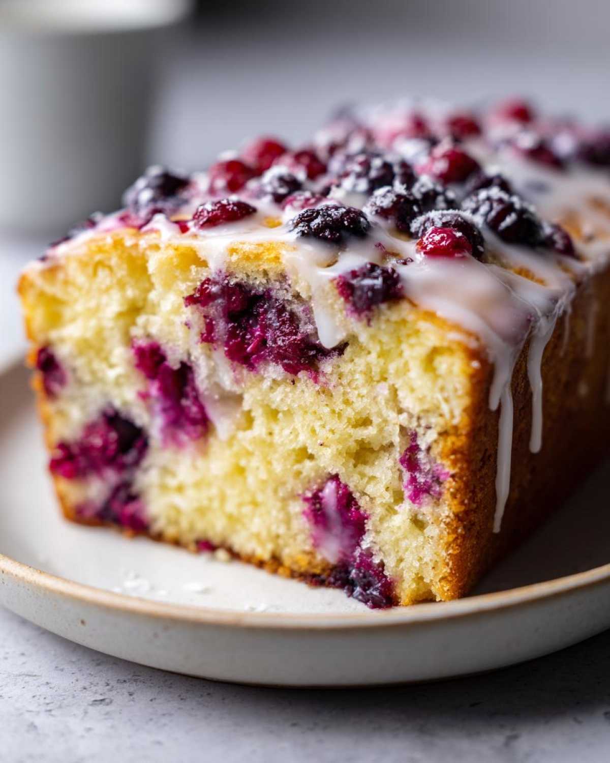 Close-up of a slice of moist Gluten-Free Lemon Berry Yogurt Cake topped with berries and a white glaze.