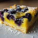 Close-up of a single serving of Gluten-Free Lemon Blueberry Layer Bars with bright yellow filling and dark blueberries, dusted with powdered sugar.