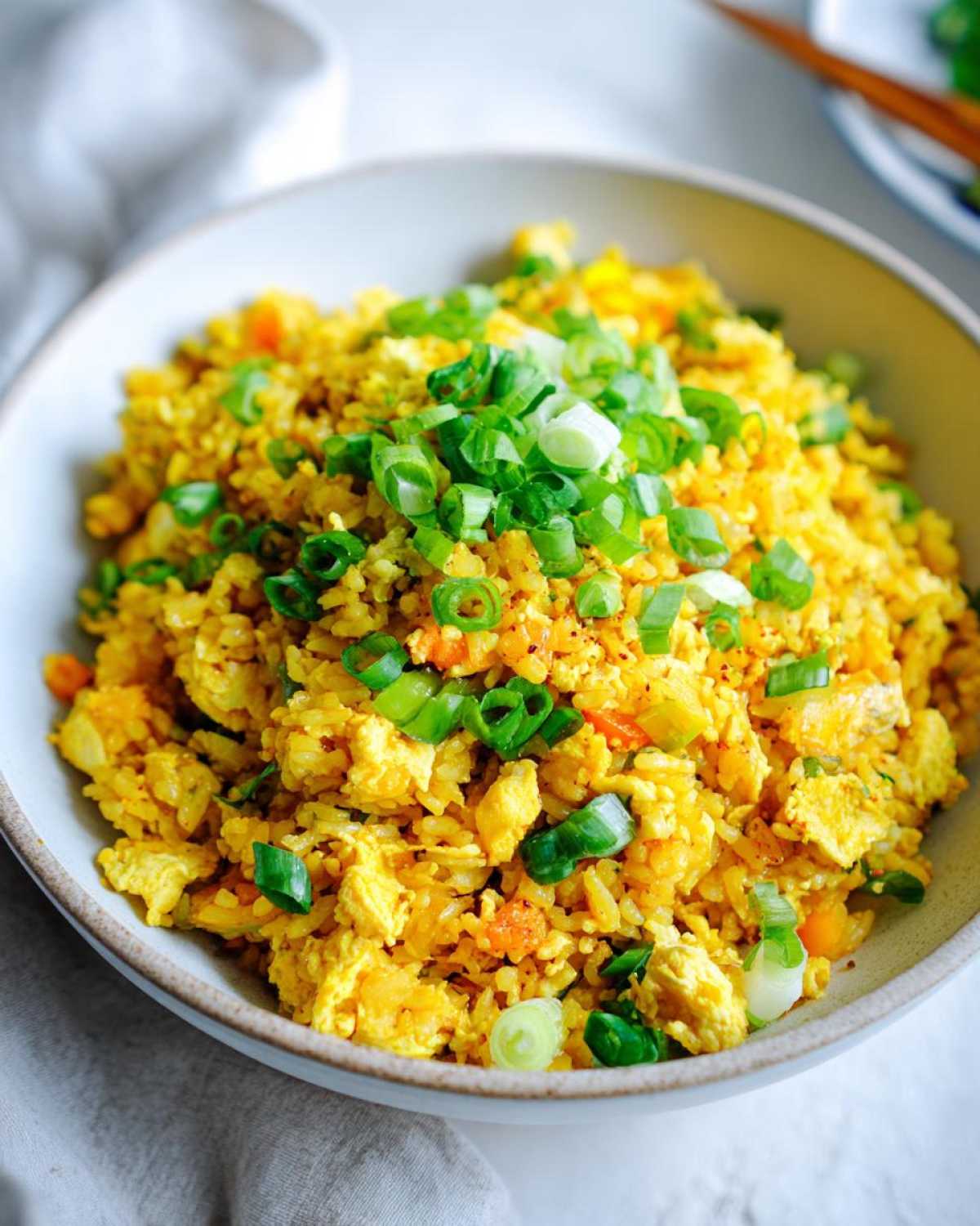 A close-up of a bowl filled with bright yellow Gluten-Free Lemon Pepper Fried Rice, topped generously with sliced green onions.