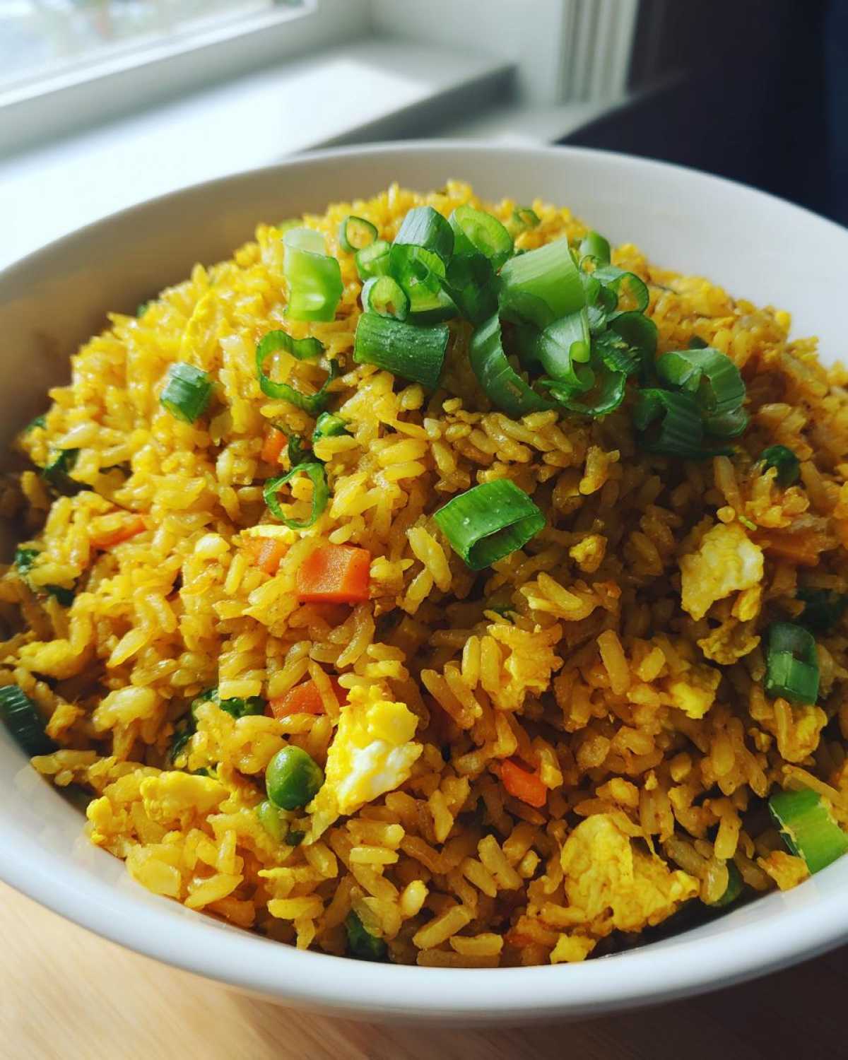 A close-up of a white bowl filled with vibrant yellow Gluten-Free Lemon Pepper Fried Rice, topped with fresh green scallions.