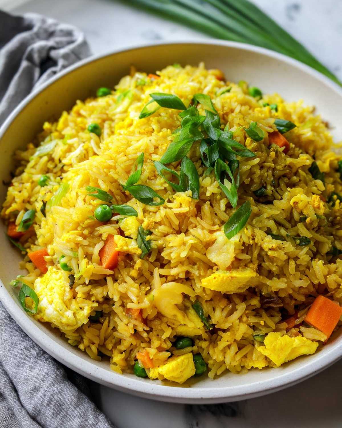 A close-up of a bowl filled with vibrant yellow Gluten-Free Lemon Pepper Fried Rice, topped with green onions.