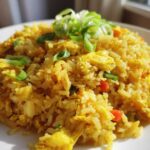 A plate piled high with vibrant yellow Gluten-Free Lemon Pepper Fried Rice, topped with fresh green scallions.