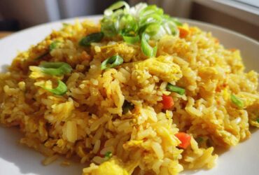 A plate piled high with vibrant yellow Gluten-Free Lemon Pepper Fried Rice, topped with fresh green scallions.