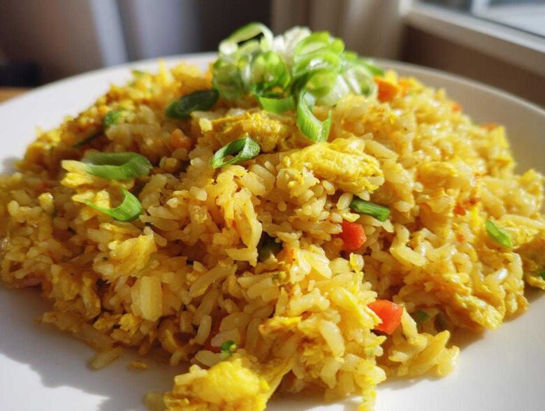 A plate piled high with vibrant yellow Gluten-Free Lemon Pepper Fried Rice, topped with fresh green scallions.