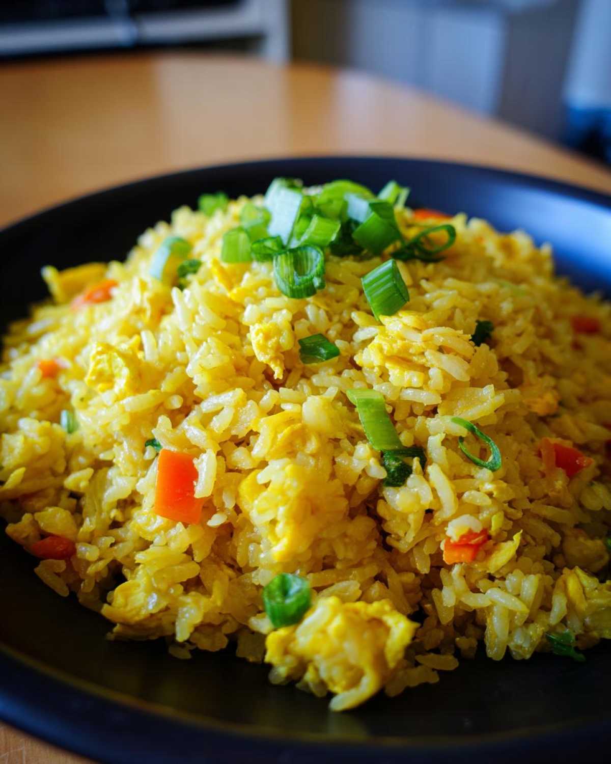 A close-up of a mound of yellow Gluten-Free Lemon Pepper Fried Rice topped with fresh chopped green onions.