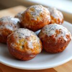 A close-up of several Gluten-Free Lemon Poppy Seed Donut Holes topped with a white lemon glaze and poppy seeds, resting on a white plate.