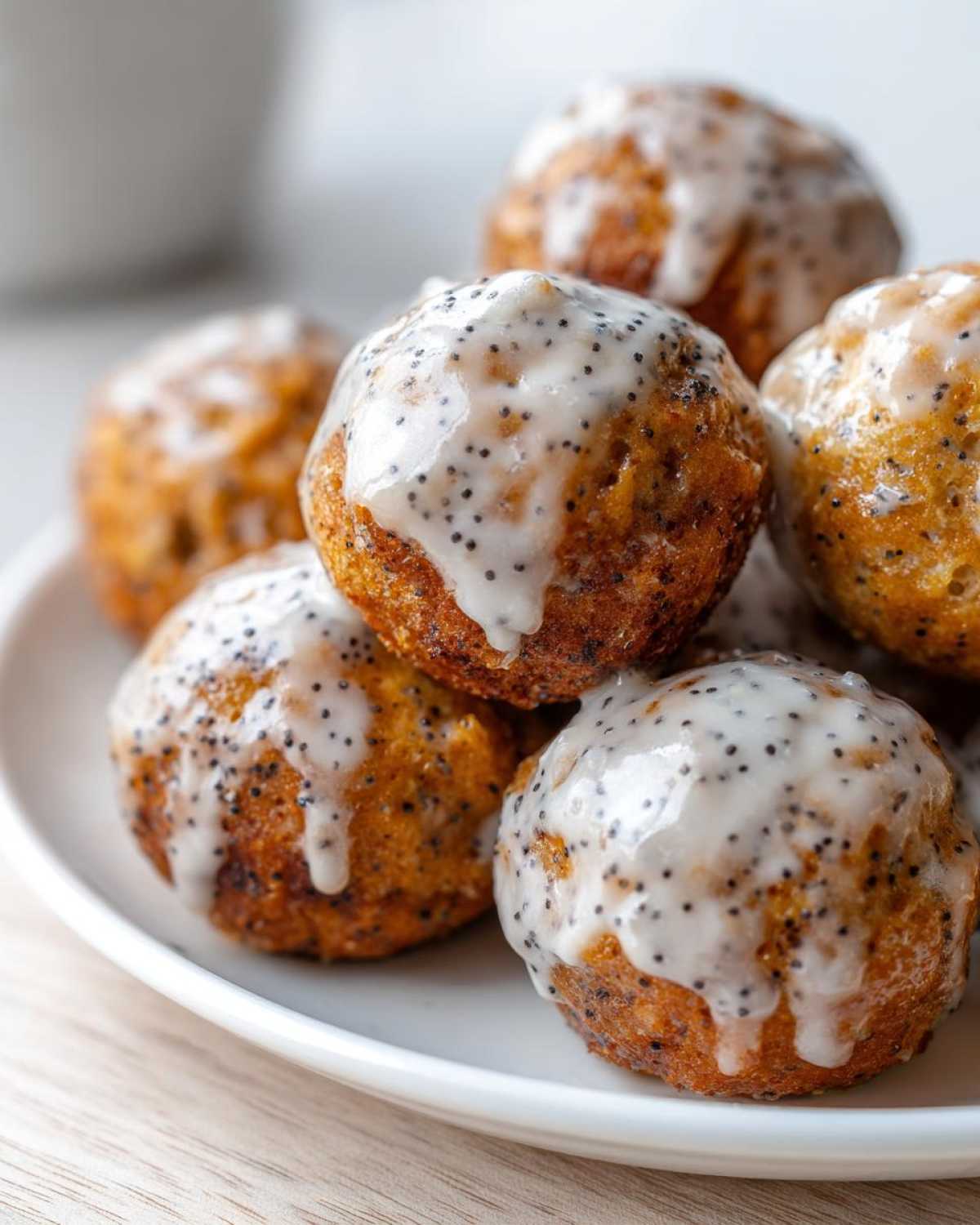 A close-up of several Gluten-Free Lemon Poppy Seed Donut Holes piled on a white plate, drizzled with a white glaze dotted with poppy seeds.