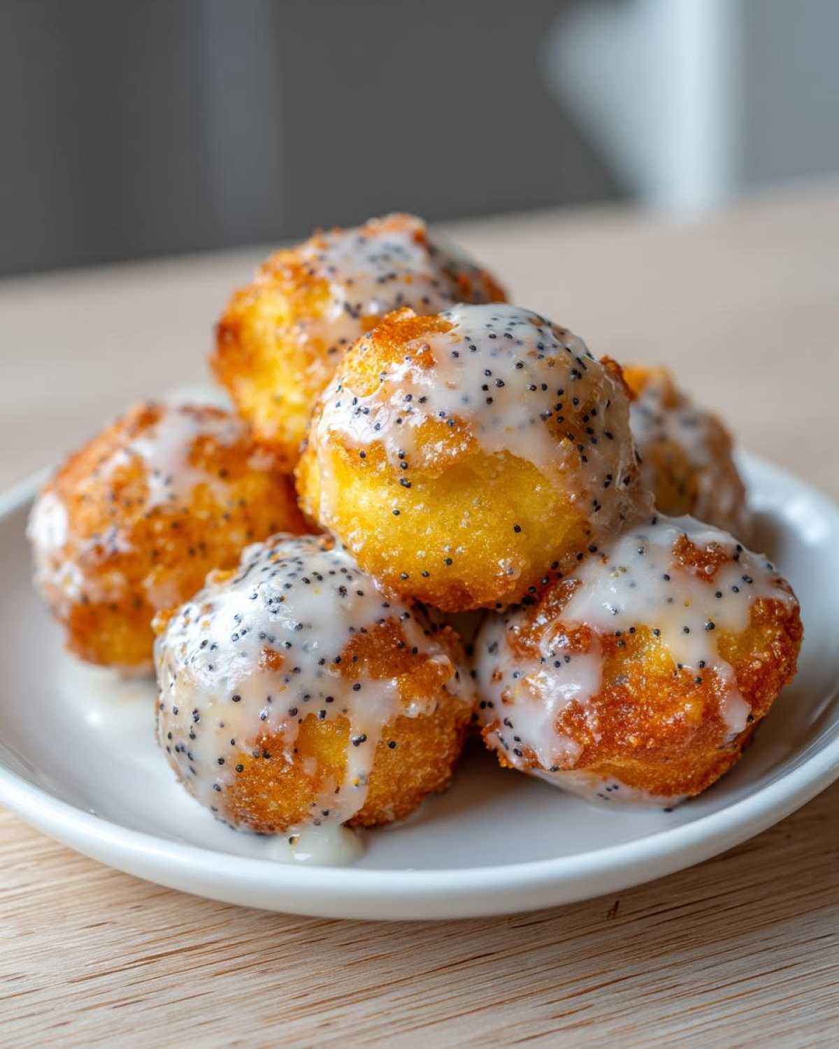 A close-up of several golden Gluten-Free Lemon Poppy Seed Donut Holes drizzled with white lemon glaze and poppy seeds.