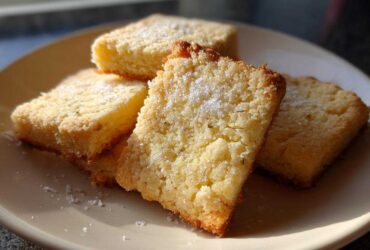 Close-up of four Gluten-Free Lemon Thyme Shortbread Cookies dusted with sugar on a light plate.