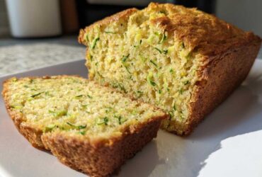 A golden-brown loaf of Gluten-Free Lemon Zucchini Bread, with two slices cut and resting against the main loaf on a white plate.