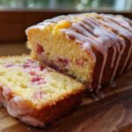 A loaf of Gluten-Free Strawberry Lemon Pound Cake, partially sliced, showing pink strawberry pieces and a lemon glaze drizzle.