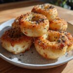 A stack of golden-brown High-Protein Cottage Cheese Bagel Bites topped with everything bagel seasoning on a speckled plate.