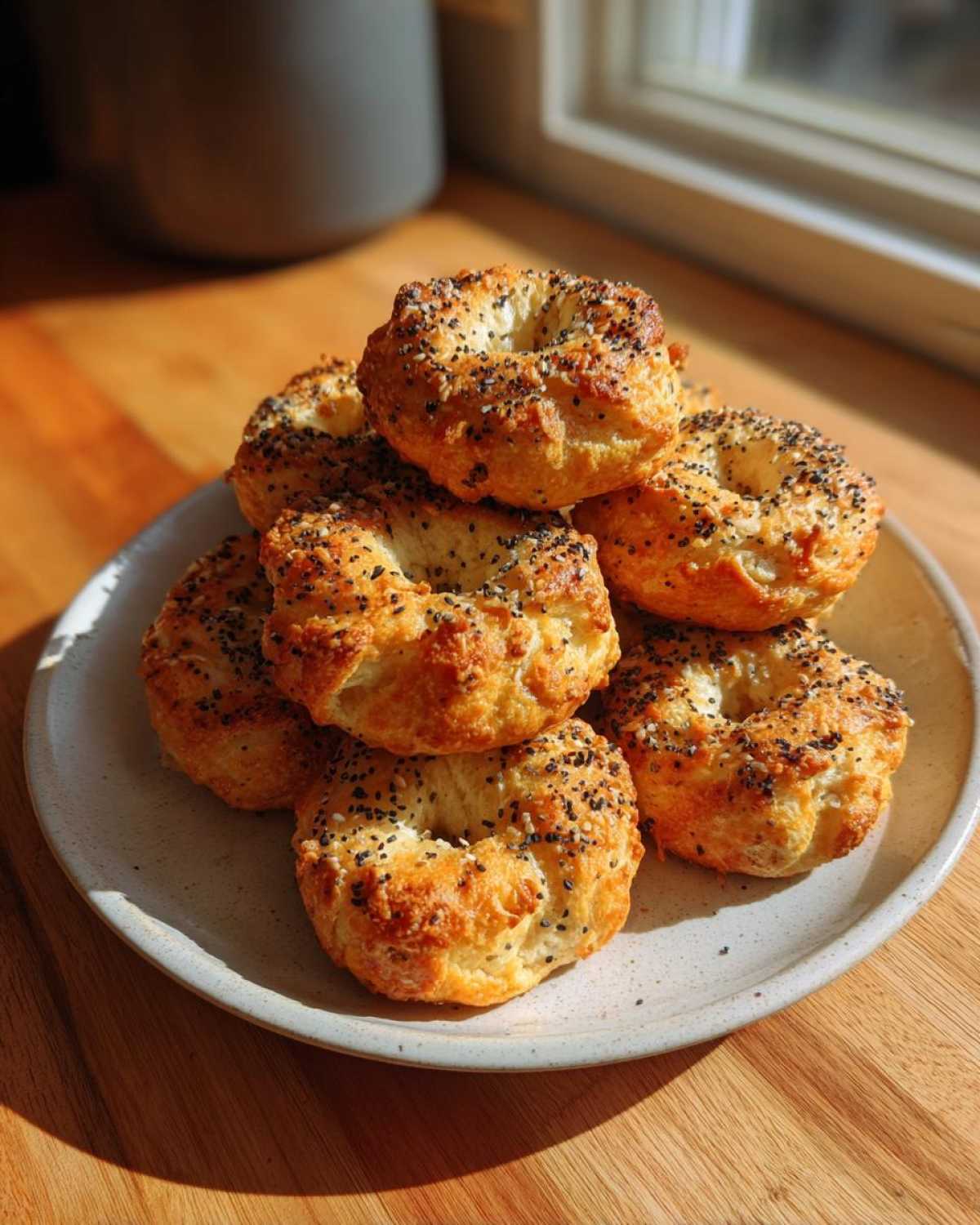 A stack of golden brown High-Protein Cottage Cheese Bagel Bites topped with everything bagel seasoning, resting on a speckled plate.