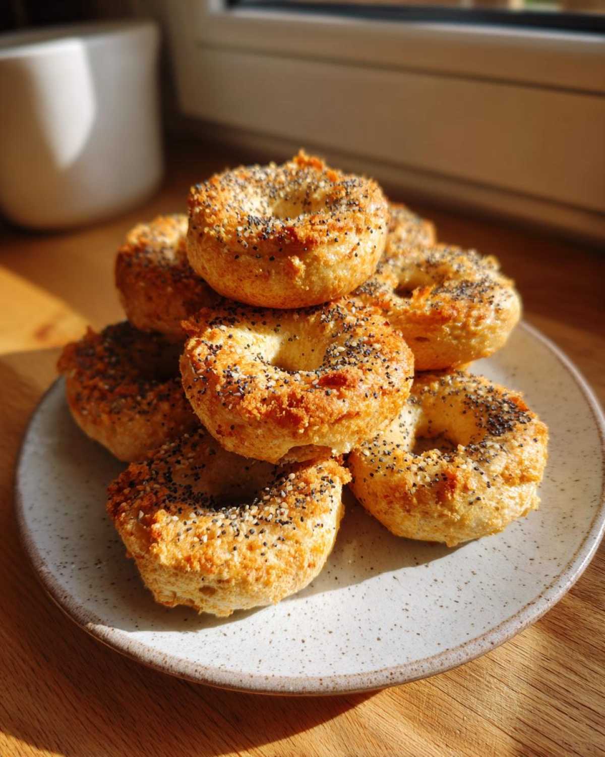 A stack of golden-brown High-Protein Cottage Cheese Bagel Bites topped with poppy and sesame seeds on a speckled plate.