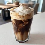 Close-up of a refreshing Iced Coconut Mocha with Cold Foam topped with whipped cream and cocoa powder.