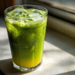 Tall glass filled with a vibrant Iced Matcha Pineapple Refresher, showing layers of green matcha and yellow pineapple juice over ice.