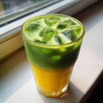 Close-up of a layered Iced Matcha Pineapple Refresher showing bright yellow juice topped with vibrant green matcha and ice.