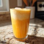 A tall glass filled with a vibrant, layered Iced Orange Creamsicle Smoothie topped with ice cubes.