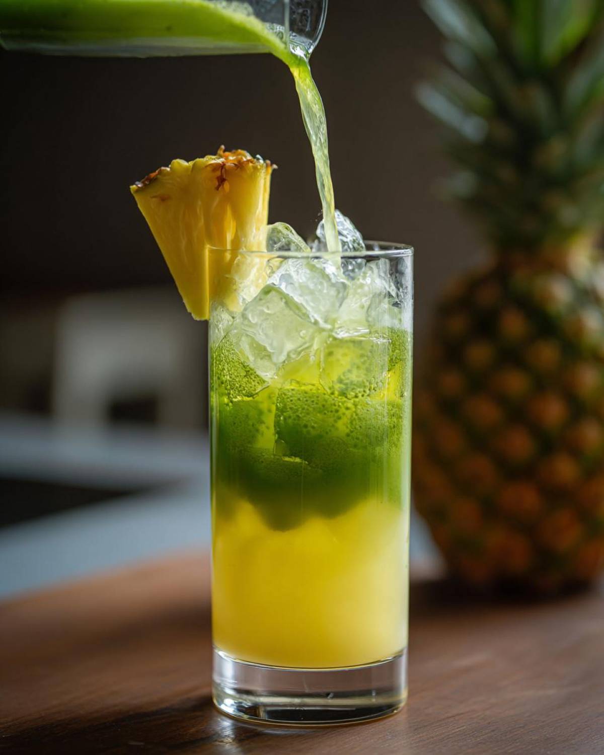 Pouring bright green matcha mixture over ice and pineapple juice to create an Iced Pineapple Matcha Spritz.