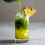Pouring bright green matcha over yellow pineapple juice and ice cubes to make an Iced Pineapple Matcha Spritz.