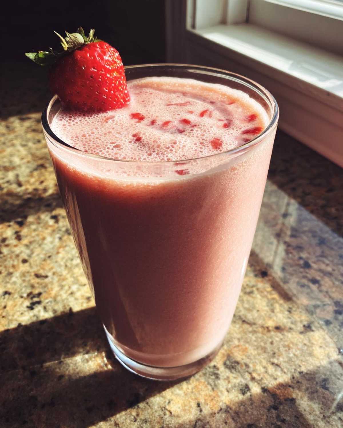 A close-up of a pink Iced Vanilla Strawberry Protein Shake garnished with a fresh strawberry.