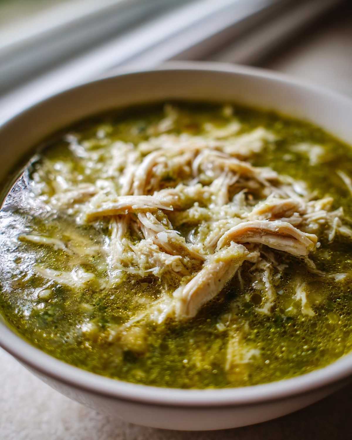 Close-up of a white bowl filled with vibrant green Instant Pot Chicken Pozole Verde soup topped with shredded chicken.