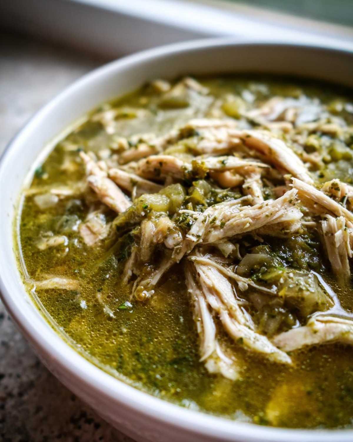 Close-up of a white bowl filled with rich green broth and shredded chicken for Instant Pot Chicken Pozole Verde.