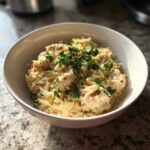 A close-up of a white bowl filled with Instant Pot Creamy Chicken and Orzo, topped with fresh parsley.