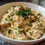 Close-up of a white bowl filled with Instant Pot Creamy Chicken and Orzo, topped with fresh parsley.