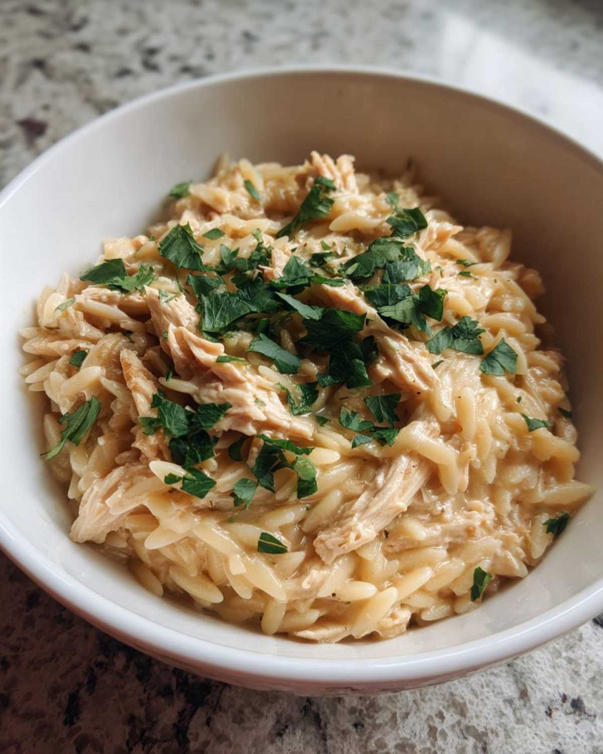 A close-up of a white bowl filled with Instant Pot Creamy Chicken and Orzo, topped with fresh parsley.