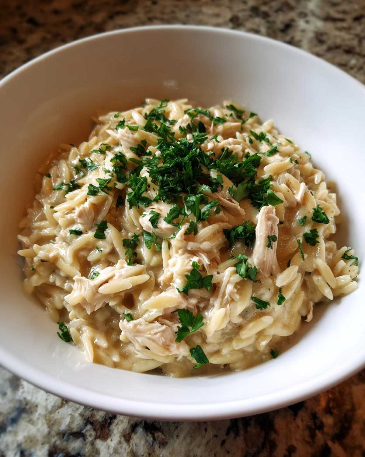 Close-up of a white bowl filled with Instant Pot Creamy Chicken and Orzo, topped with fresh parsley.