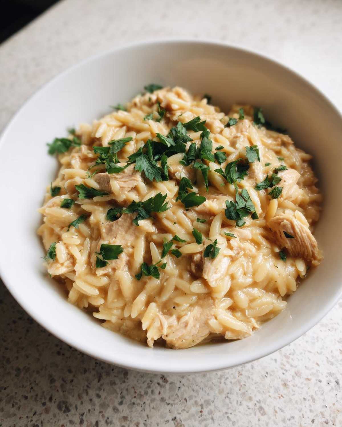 A close-up of Instant Pot Creamy Chicken and Orzo served in a white bowl and garnished with fresh parsley.