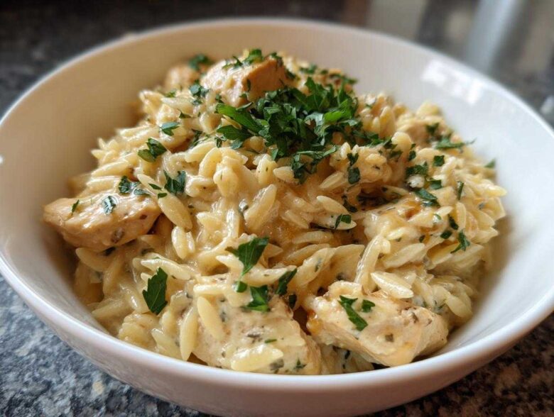 Close-up of a white bowl filled with Instant Pot Creamy Chicken and Orzo, topped with fresh parsley.