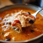 A spoonful of rich, orange Instant Pot Creamy Chicken Enchilada Soup showing shredded chicken, black beans, and melted cheese.