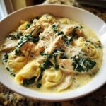 A close-up of Instant Pot Creamy Chicken Tortellini Soup featuring tortellini, shredded chicken, spinach, and grated Parmesan cheese.
