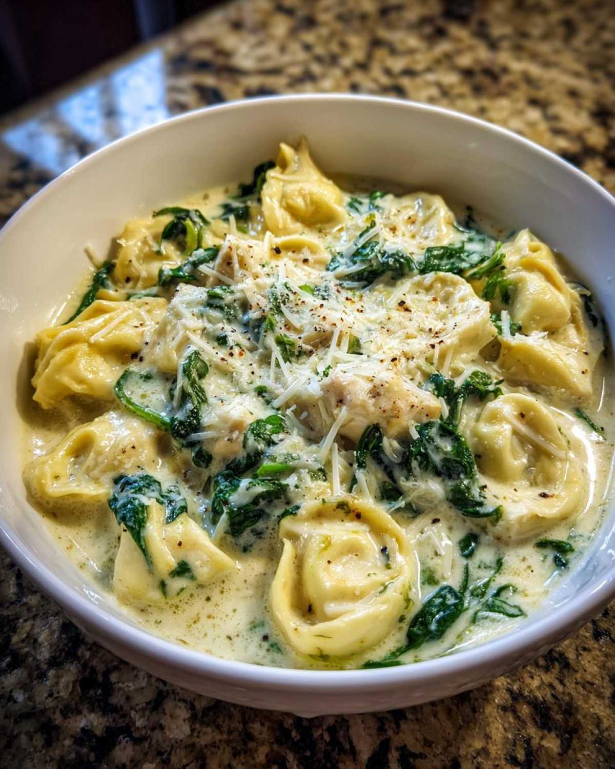 A close-up of a white bowl filled with Instant Pot Creamy Chicken Tortellini Soup, topped with Parmesan cheese.