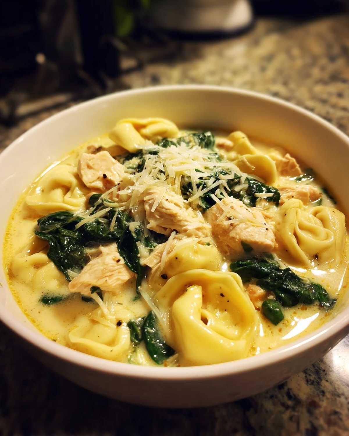 A close-up of a white bowl filled with Instant Pot Creamy Chicken Tortellini Soup, topped with shredded cheese.