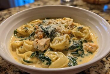A close-up of a white bowl filled with Instant Pot Creamy Chicken Tortellini Soup, featuring tortellini, chicken chunks, spinach, and grated Parmesan.