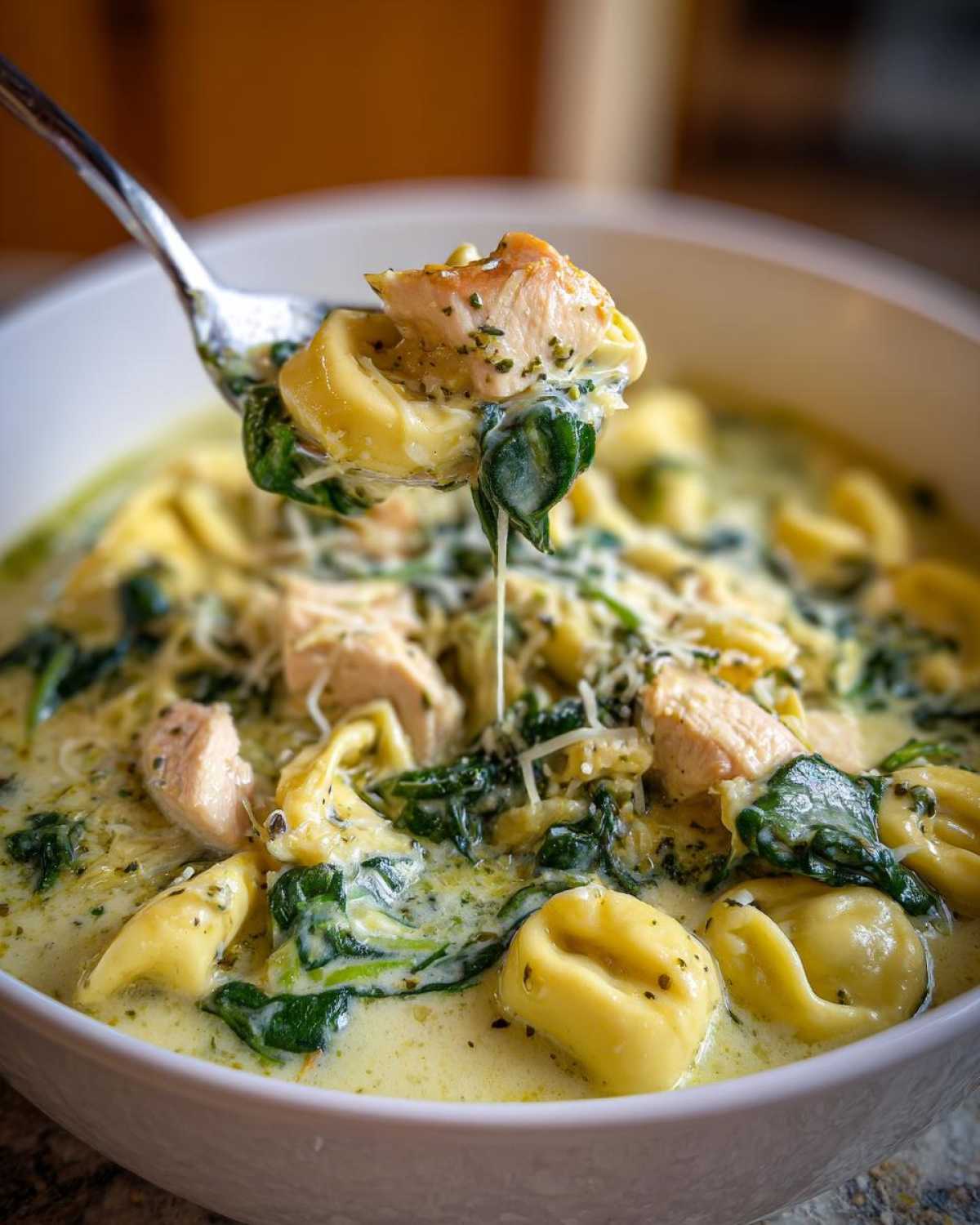 A spoonful of Instant Pot Creamy Chicken Tortellini Soup showing chicken, spinach, and tortellini being lifted from the bowl.