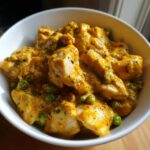 Close-up of chunks of chicken coated in rich, yellow Instant Pot Creamy Coconut Chicken Curry sauce with green peas.