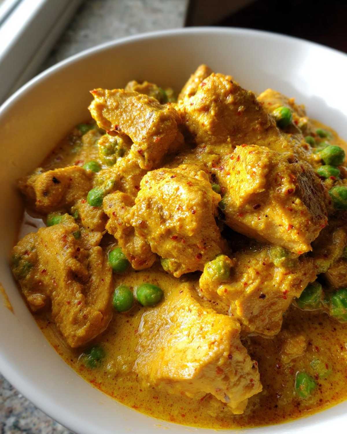 Close-up of Instant Pot Creamy Coconut Chicken Curry with chunks of chicken and green peas in a rich yellow sauce.