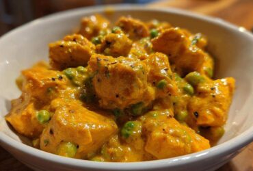 A close-up bowl of vibrant orange Instant Pot Creamy Coconut Chicken Curry with green peas.