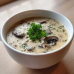 A close-up of Instant Pot Creamy Mushroom Barley Soup, garnished with fresh parsley, served in a white bowl.