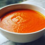 Close-up of a white bowl filled with vibrant orange Instant Pot Creamy Red Pepper Tomato Soup.