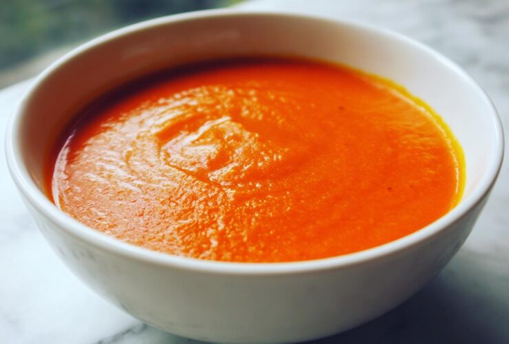 Close-up of a white bowl filled with vibrant orange Instant Pot Creamy Red Pepper Tomato Soup.