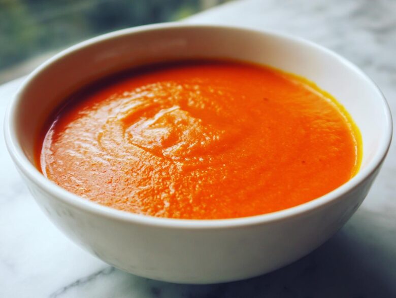 Close-up of a white bowl filled with vibrant orange Instant Pot Creamy Red Pepper Tomato Soup.
